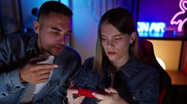 Odaklanmış bir adam ve kadın gece vakti neon ışıklı bir oyun odasında oyun oynuyorlar..