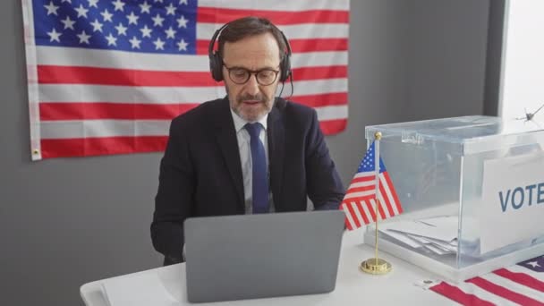 在美国的投票中心 一个拿着耳机 拿着笔记本电脑 拿着国旗和投票箱的成熟男人 — 图库视频影像