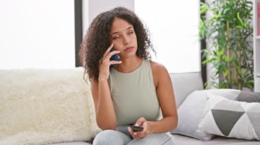 Evde gevşemiş, genç, İspanyol bir kadın TV izlerken telefonda ciddi bir konuşma yapıyor.