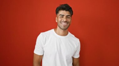 Beyaz gömlekli yakışıklı İspanyol adam kırmızı duvara karşı duruyor, farklı duygular ifade ediyor..