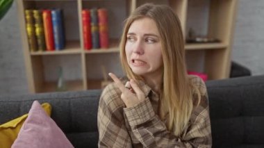 Sersemledim! Genç sarışın kadın, endişeli bir şekilde evinde oturuyor, şok olmuş bir ifadeyle, endişeli işaret parmağını inançsızlığa doğrultuyor..