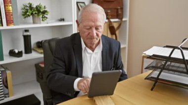 Kendinden emin ve neşeli kıdemli bir adam, beyaz saçlı akılda kalıcı bir patron, zarif ofis masasında dokunmatik dokunmatik pedini kullanarak mutlu bir şekilde çalışıyor, her gülüşünde başarı yayıyor..