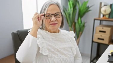 Modern ofiste gülümseyen gözlüklü kendinden emin yaşlı kadın.