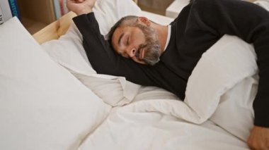 Gri sakallı olgun bir adam yatak odasında huzur içinde uyur. Rahatlık ve rahatlık uyandırır..