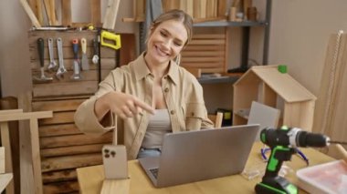 Neşeli genç sarışın kadın marangozluk fikrini heyecanla sunuyor atölyede dizüstü bilgisayara gülümserken kendinden emin bir şekilde işaret ediyor.