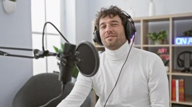 Genç, yakışıklı İspanyol adam, neşeyle ışıldıyor, radyo stüdyosunun içinde kulaklıklarıyla dinlerken havalı bir 