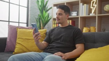 Modern oturma odasında akıllı telefon kullanan İspanyol adam heyecan ve neşe gösteriyor..
