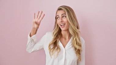 Tişörtlü neşeli sarışın kadın yukarı bakıyor, parmakları pembe izole edilmiş arka planda dört numarayı gösteriyor.