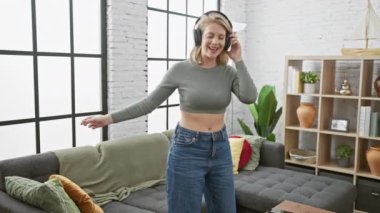 Genç bir kadın modern bir oturma odasında neşeyle dans ediyor, kulaklık takıyor, evde rahatlık ve rahatlık yayıyor..