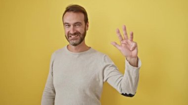Neşeli orta yaşlı İspanyol adam, 4 numarayı sembolize ediyor, güneşli sarı bir duvara karşı izole bir şekilde gülümsüyor..