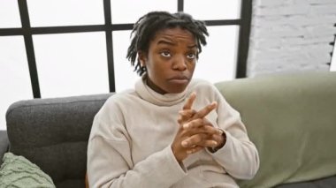 Kanepede oturan depresif, siyah bir kadın, yukarıyı işaret ediyor. Üzüntü ve ızdırapla bir yön gösteren, duygusal bir Afrikalı Amerikalı kadının mutsuz bir portresi.