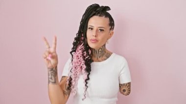 Neşeli İspanyol ampüte kadın zafer işareti gösteriyor, pembe izole edilmiş arka planda göz kırpıyor ve gülümsüyor.