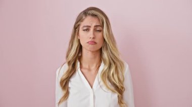 Üzgün, genç, sarışın bir kadın, yönü aşağı doğru gösteren, gömlek giyen, mutsuz, üzgün ve depresif, izole pembe bir duvar üzerinde duran.