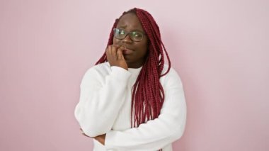 Gözlüklü ve pembe arka planda beyaz süveter giyen düşünceli Afrikalı kadın.