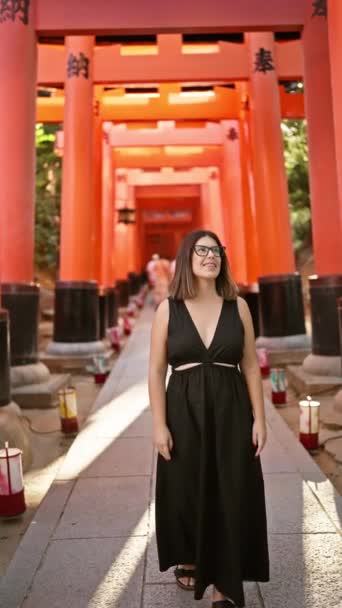 メガネでヒスパニックな美しさを確信し 耳から耳まで研ぎ澄み 京都のオレンジ色の鳥居トンネルで畏敬の念を抱いて周りを見渡す — ストック動画