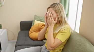 Depresyon kaplıyor, genç, sarışın kadın evde ağlıyor, elleri yüzünü kaplayan üzüntü ifadesi. Ondan yayılan huzursuzluk,