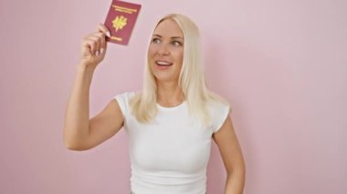 Neşeli sarışın bayan Fransa pasaportunu gösteriyor, pembe izole bir arka planda baş parmağıyla gülümsüyor.