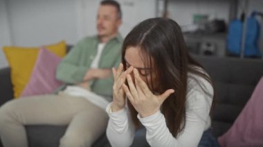 Üzgün bir kadın ve ilgisiz bir adam modern bir oturma odasında bir kanepede oturuyorlar.