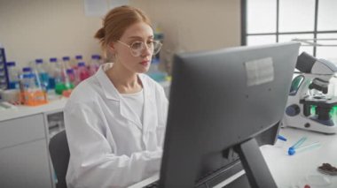 Gözlüklü beyaz bir kadın bilim adamı laboratuardaki bir bilgisayardaki verileri inceliyor..