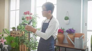 Asyalı bir adam çiçekçide çiçek düzenliyor bir dizi bitki ve bahçe aletleri ile.