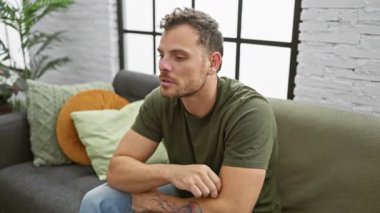 Evde şok olmuş genç bir adam, elleri inançsızlıkla ağzını kapatıyor. Kanepede şokla otururken yaptığı gizli hatadan korktu..