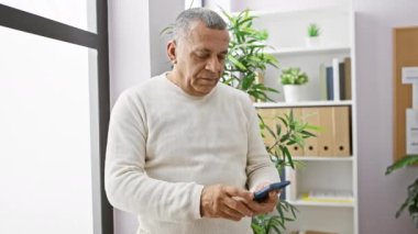 Modern ofiste akıllı telefon kullanan olgun bir İspanyol..