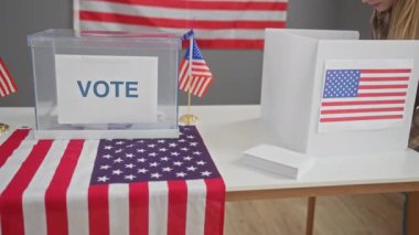 Yıldız ve şeritlerle süslenmiş bir Amerikan seçim merkezinde genç bir kadın oy kullanıyor.