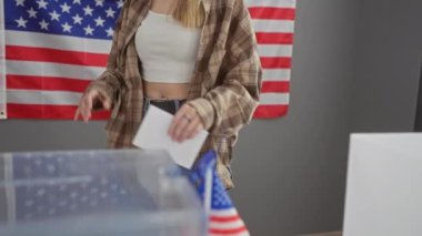 Genç sarışın kadın Amerikan bayraklarıyla Amerikan seçim bölgesinde oy kullanıyor.