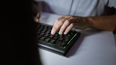 Karanlık bir odada arka ışıklandırılmış mekanik bir klavyeye yazarak teknolojiyi ve işi ön plana çıkaran bir adamın ellerine yakın çekim..