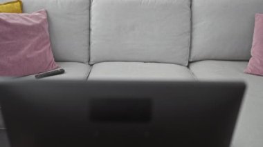 Orta yaşlı bir kadın rahat bir oturma odasında kanepede oturuyor. Akıllı telefon ve uzaktan kumanda kullanıyor.