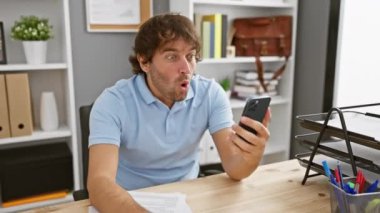 Şok olmuş Kafkasyalı genç ofis çalışanı aptal, şaşkın bir ifadeyle ağzı tamamen açık bir şekilde kapalı bir şekilde akıllı telefonuna yapışmış vaziyette ürkmüştü.!