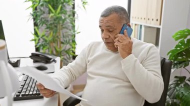 Ofisteki İspanyol adam belgeleri incelerken telefonla konuşuyor.