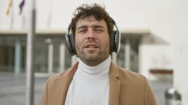 Genç bir İspanyol, şehir sokak ortamında kulaklıklarla müzik dinliyor, gözleri kapalı ve memnun..