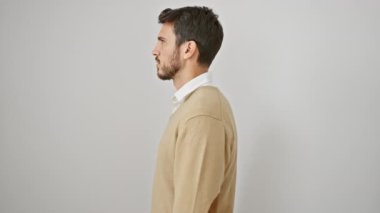 Beyaz izole edilmiş arka planda duran, kendine güvenen genç, İspanyol bir adam, doğal bir şekilde gülümsüyor, rahat bir yan profil pozu veriyor.