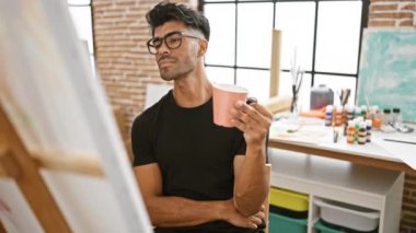 Düşünceli, sakallı, genç bir İspanyol, bir sanat stüdyosunda pembe kupa tutuyor..