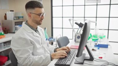 Modern laboratuarda bilgisayar üzerinde çalışan laboratuvar önlüklü yakışıklı İspanyol bilim adamı.