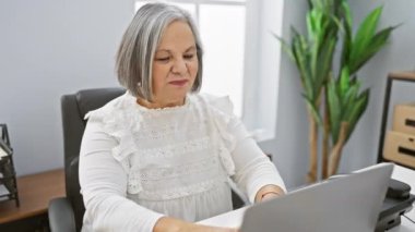 Modern ofis ortamında dizüstü bilgisayarla çalışırken boynu ağrıyan olgun bir kadın..