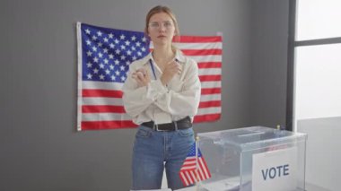 Çapraz kollu kendine güvenen genç bir kadın Amerikan demokrasisini sembolize eden ABD bayrağı ve oy sandığıyla bir seçim merkezinde duruyor..