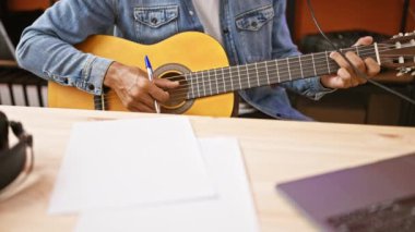 Stüdyoda dizüstü bilgisayarı ve gitarıyla müzik yapan genç bir İspanyol..