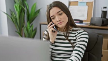 Ofisteki genç bir İspanyol kadın telefonla konuşuyor, profesyonellik yayıyor ve teknolojik ve idari çevreye odaklanıyor..