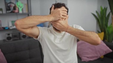 Orta yaşlı bir adam, komik ama yine de şokta. Beyaz bir tişörtle yüzünü kapatıyor. Şaşırdığını ve gizli duygularını ifade ediyor..