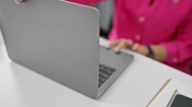 Modern beyaz ofis masasında dizüstü bilgisayarda çalışan pembe bluzlu beyaz bir kadın. Akıllı telefon ve not defteriyle.