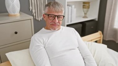 Neşeli, gri saçlı, orta yaşlı pijamalı bir adam, sıcak bir yatak odasından 