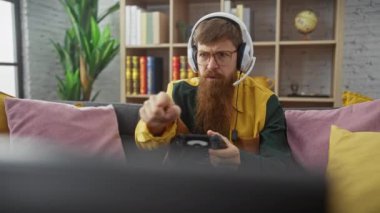 Kulaklıklı sakallı bir adam ev ortamında yoğun bir şekilde video oyunları oynar..