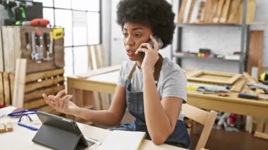Bir atölyede telefon ve tablet kullanarak birden fazla iş yapan odaklanmış bir kadın marangoz..