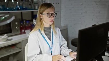 Laboratuvar önlüklü, yorgun, beyaz bir kadın bilim adamı laboratuvar ekipmanlarının arasında çalışma yerinde geriliyor..