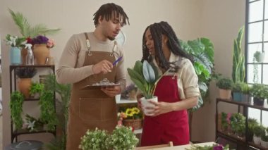 Bir erkek ve bir kadın, her ikisi de çiçekçi, bereketli çiçeklerle çevrili canlı bir çiçekçide iş birliği yapıyorlar.