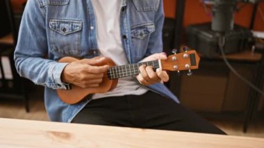 Kot ceketli yakışıklı bir İspanyol, bir müzik stüdyosunda ukulele çalıyor.