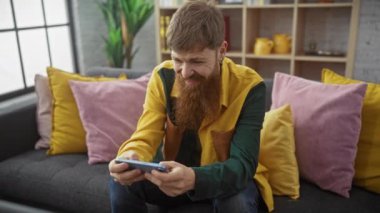 Sakallı adam, canlı ev içinde akıllı telefonuyla oynarken kutlama yapıyor..