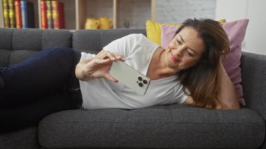 Neşeli bir İspanyol kadın evinde bir kanepeye uzanır, akıllı telefonuyla meşgul olur, rahat bir güzellik ve rahatlama hissi yayar..